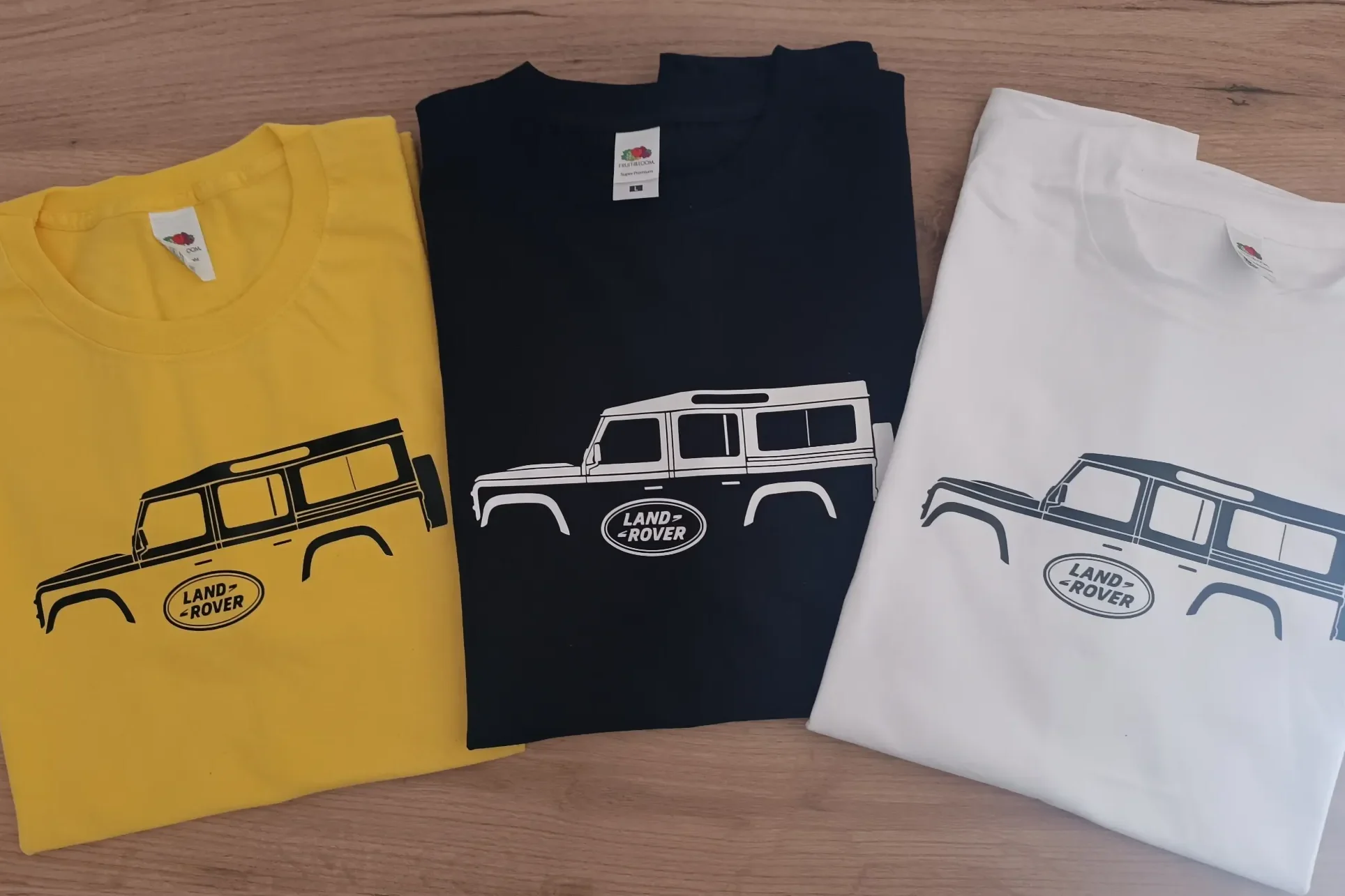 Auto T-Shirts Drei T-Shirts in Gelb, Schwarz und Weiß mit einem Land Rover Defender 110 in Schwarz.