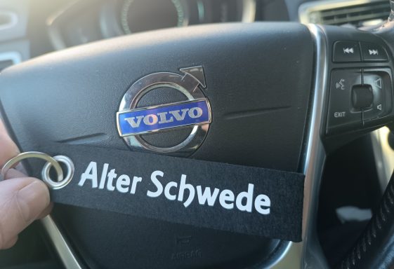 Schlüsselanhänger Alter Schwede Volvo-Logo auf einem Lenkrad mit einem Schlüsselanhänger mit der Aufschrift "Alter Schwede".